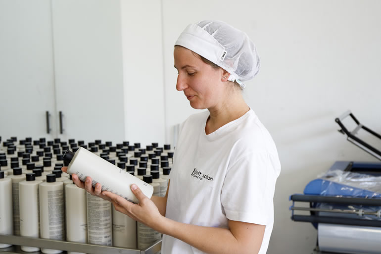Сотрудница Дотт Солари проверяет бутылку косметики, контроль качества на производстве.